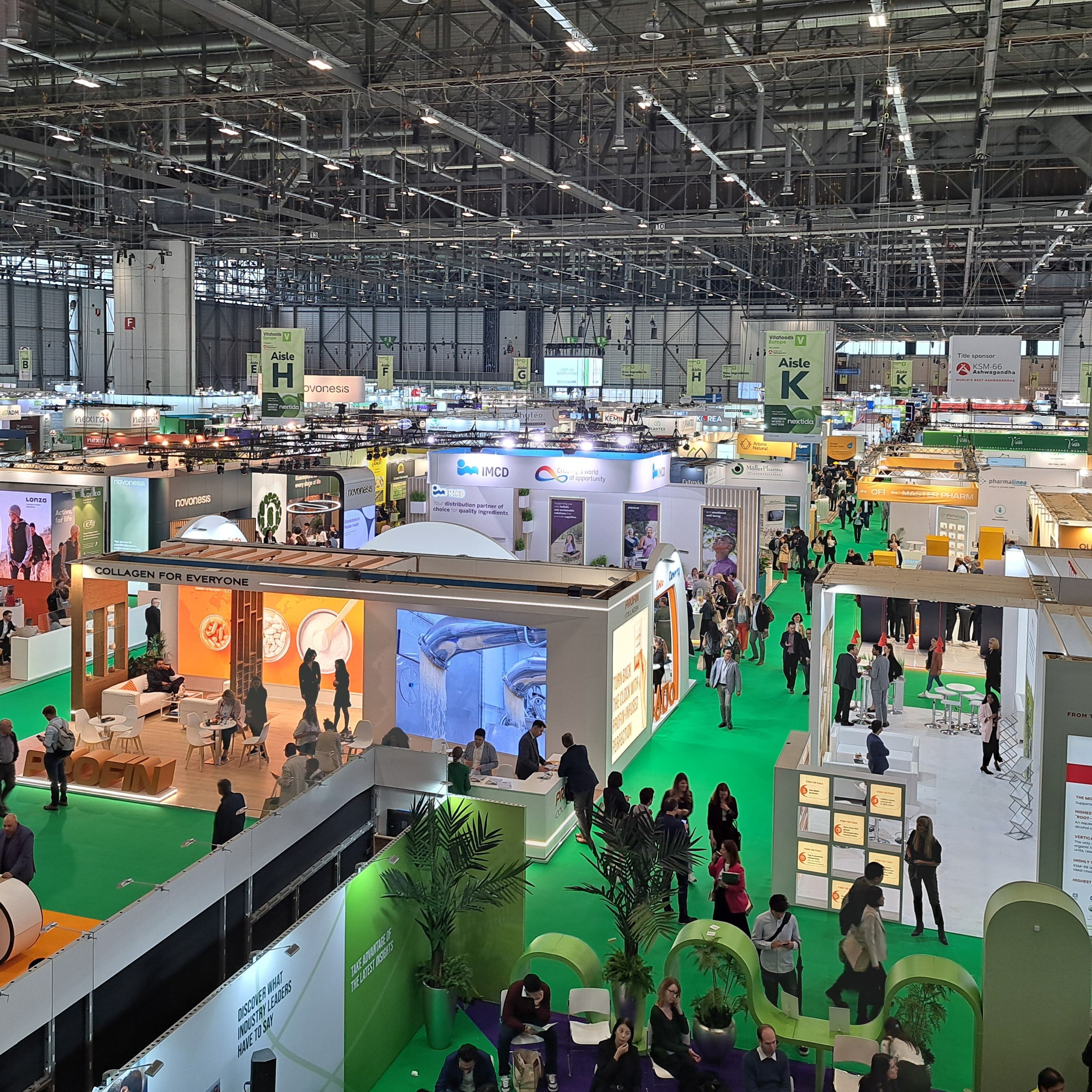 <Looking down at a large supplier exhibition with square supplier stands and green walkways between them. Credit> GMP-SOP-Download @ Vitafoods