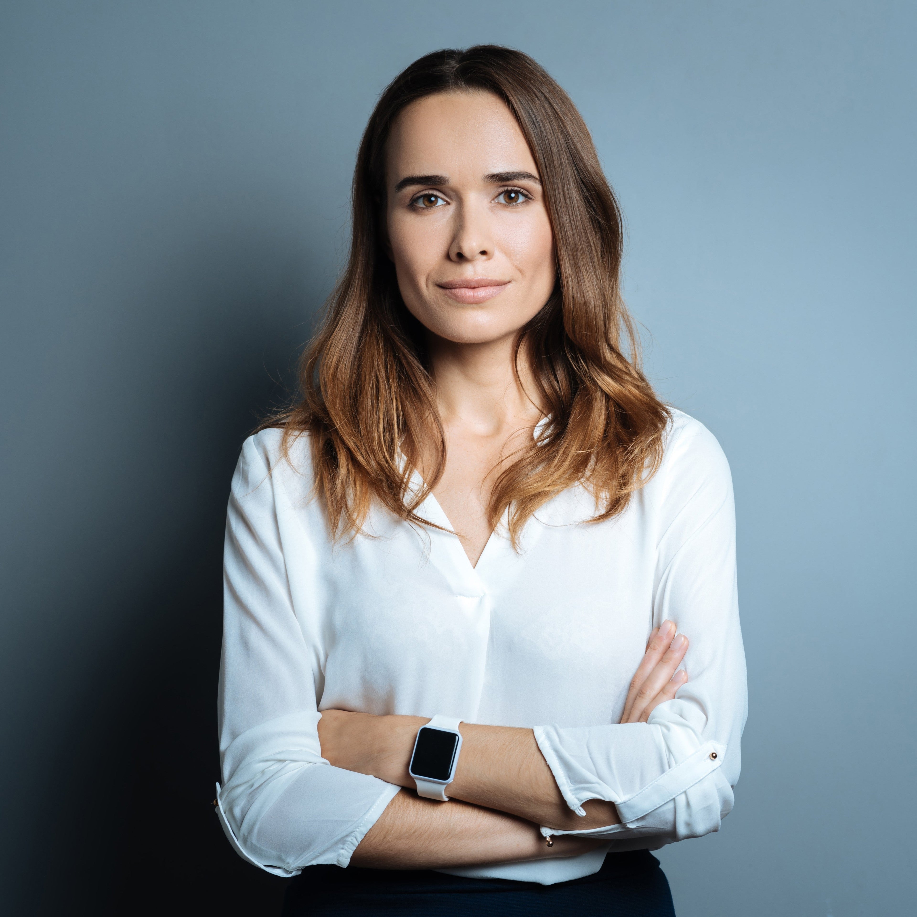 <Female manager wearing white shirt and i-watch in corporate pose with arms folded against a grey wall. Credit> AdobeStock_170931593