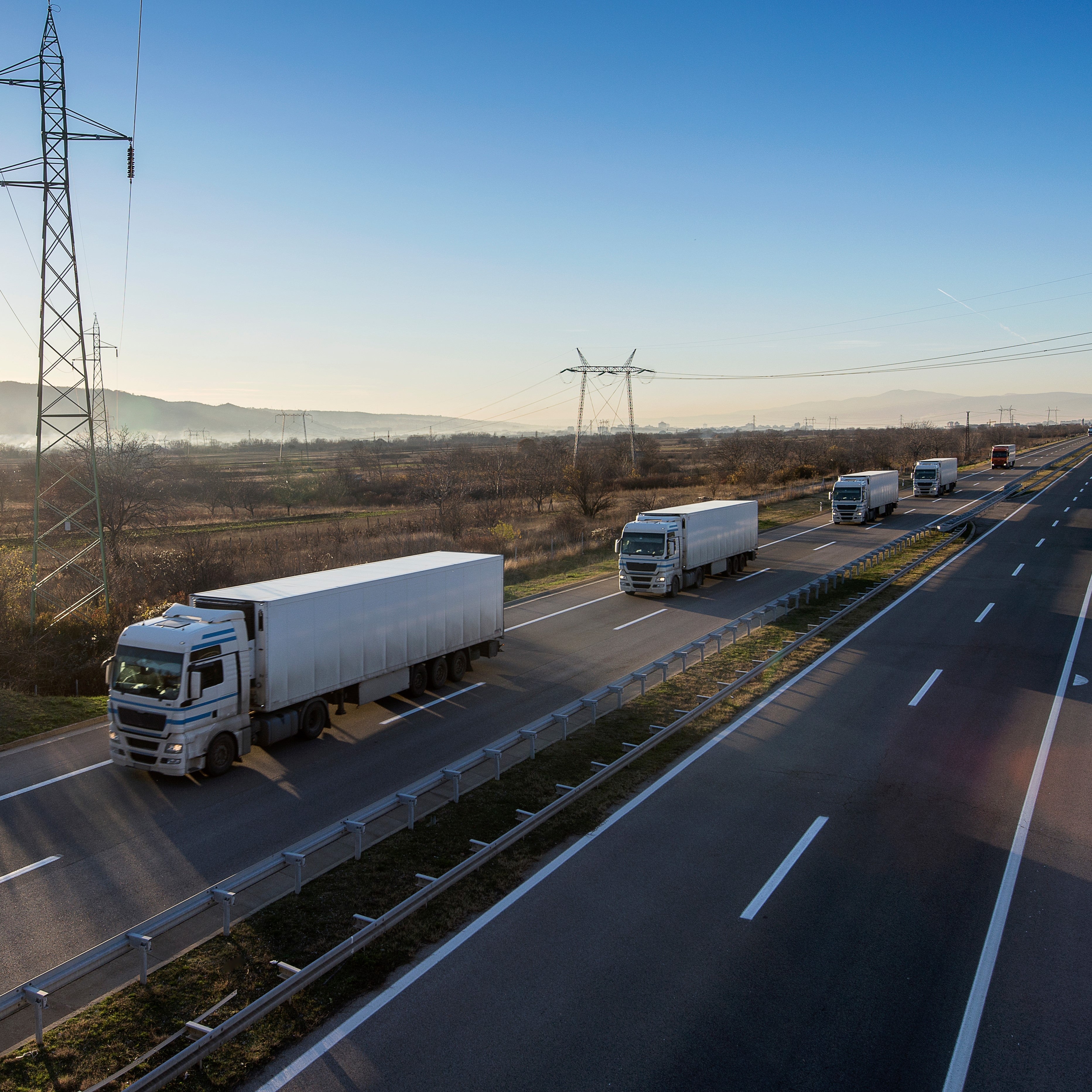 <Convoy of white lorries distributing drug products on an empty motorway in early morning sunlight. Credit> AdobeStock_464144081