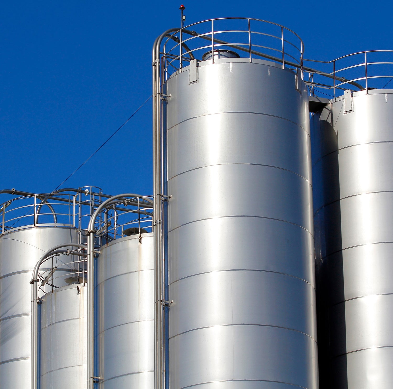 &lt;Five, tall,  large cylindrical, stainless steel silo tanks with a blue sky behind them for receipt and storage of liquid dietary supplement ingredients. Credit&gt; AdobeStock_102652410