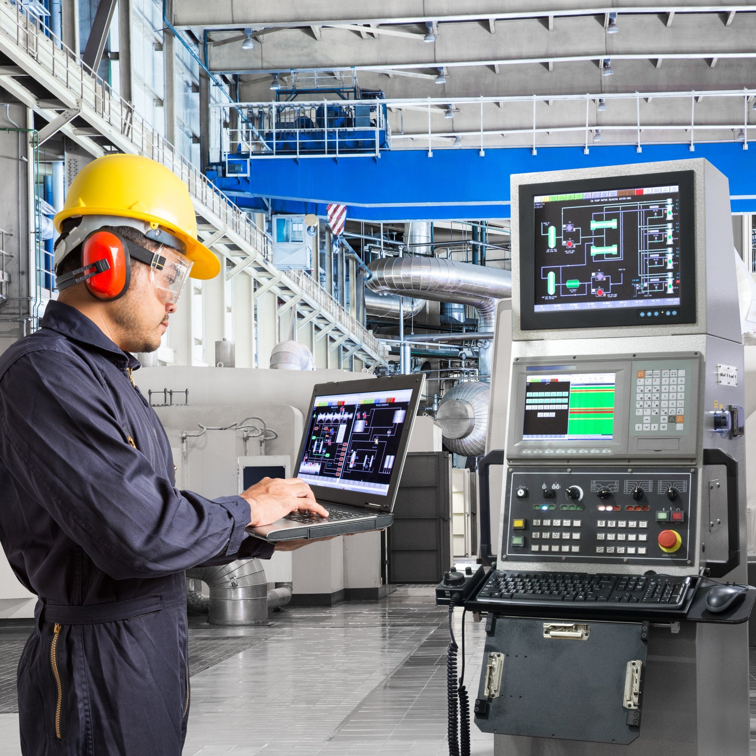 &lt;Maintenance Engineer wearing blue overalls, yellow hard hat, safety glasses, and orange ear defenders stood in a large open production area diagnosing an electrical fault on a control panel with a laptop computer. Credit&gt; AdobeStock_133613247