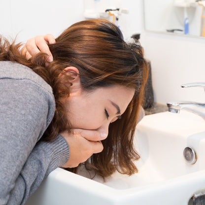 &lt;Chinese female employee with auburn coloured hair, wearing a grey jumper, off work sick holding her mouth leaning into a white bathroom sink below a mirror about to vomit, Credit&gt; AdobeStock_137810648