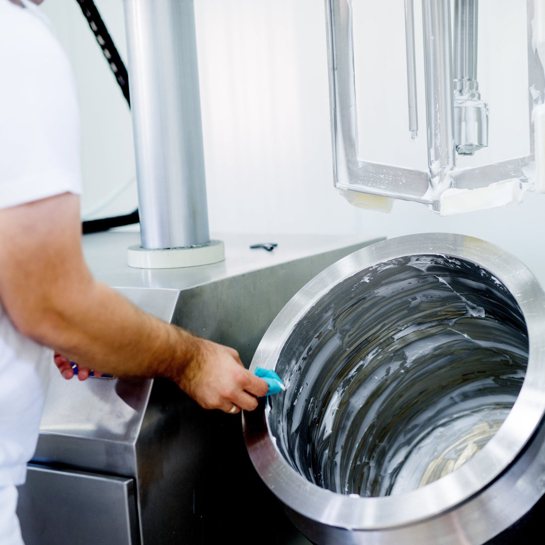 &lt;Production operator wearing white cleaning a stainless steel mixing bowl, which has been used to manufacture liquid dietary supplements, in a white walled production area. Credit&gt; AdobeStock_166858201