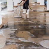 <Legs of a man wearing black trousers and white wellington boots pressure washing the concrete walkway of an employee parking lot to remove oil and dirt. Credit> AdobeStock_169381335