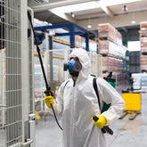 <Qualified pest control expert with full white protective clothing, chemical mask, and yellow gloves, spraying an infestation in some empty racking in the warehouse away from materials and product. Credit> AdobeStock_170118869