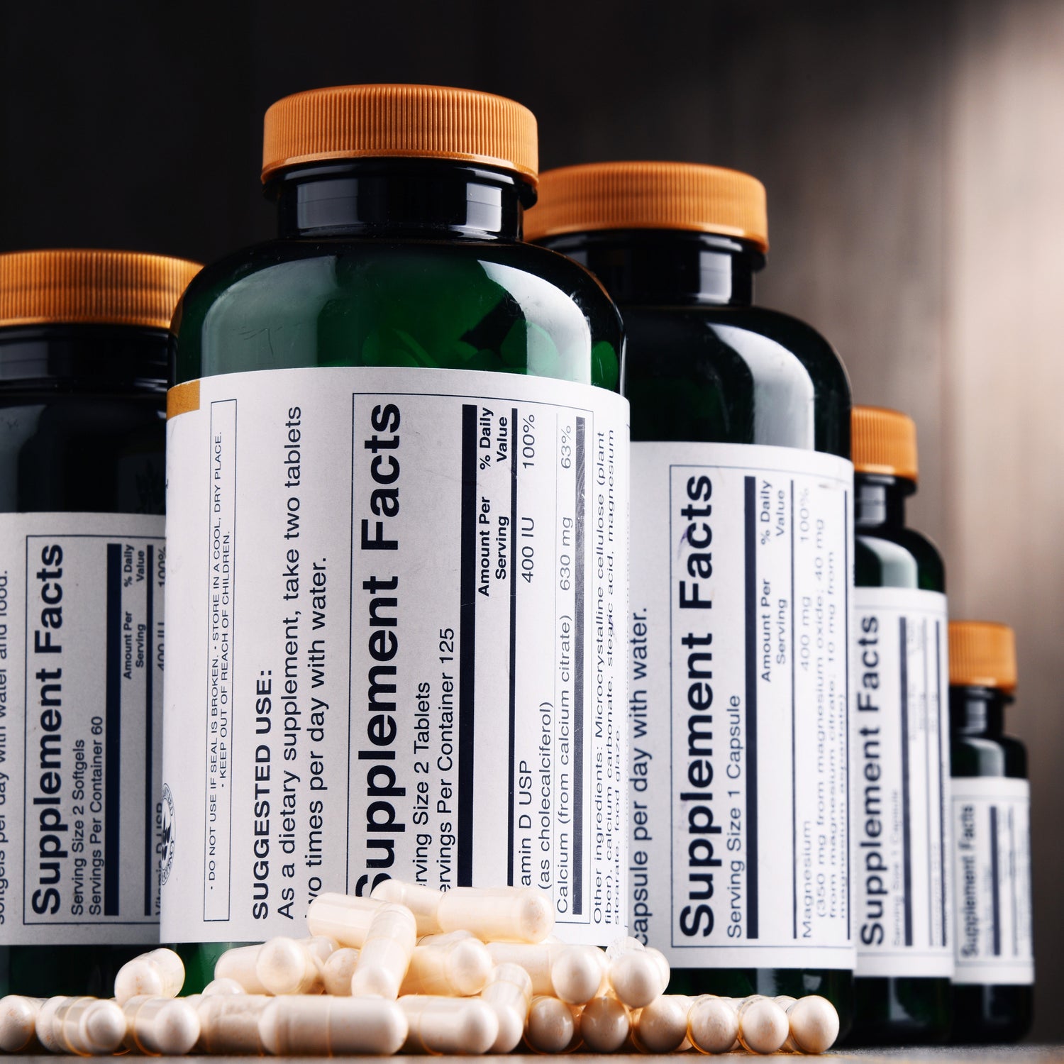 &lt;White capsules on a table in front of amber brown plastic bottles with supplement facts labels, an example of which is one of the requirements of a batch production record for dietary supplements. Credit&gt; AdobeStock_175842025