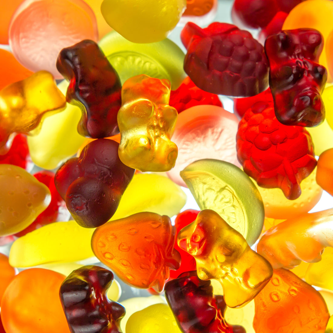 &lt;Close up view of bear and fruit shaped purple, green, red, and yellow dietary supplement gummies spread out on a bright white light shining through them. Credit&gt; AdobeStock_195059540