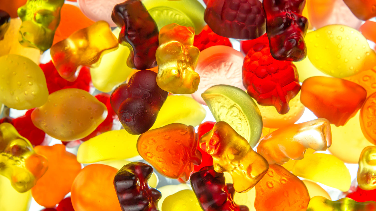 &lt;Yellow, orange, green, red and purple gummies in the shape of fruits or teddy bears spread on a white light source making them appear transparent. Credit&gt; AdobeStock_195059540