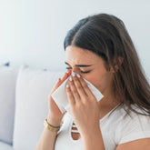 <Employee at home sitting on a white sofa, off work sick with cold and flu, staying at home to prevent spreading and cross-contamination from sneezing. Credit> AdobeStock_219422085