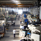 <Looking down at a distribution area of a warehouse with several employees walking down a central aisle and others working at stations packing boxes for dispatch. Credit> AdobeStock_250623771