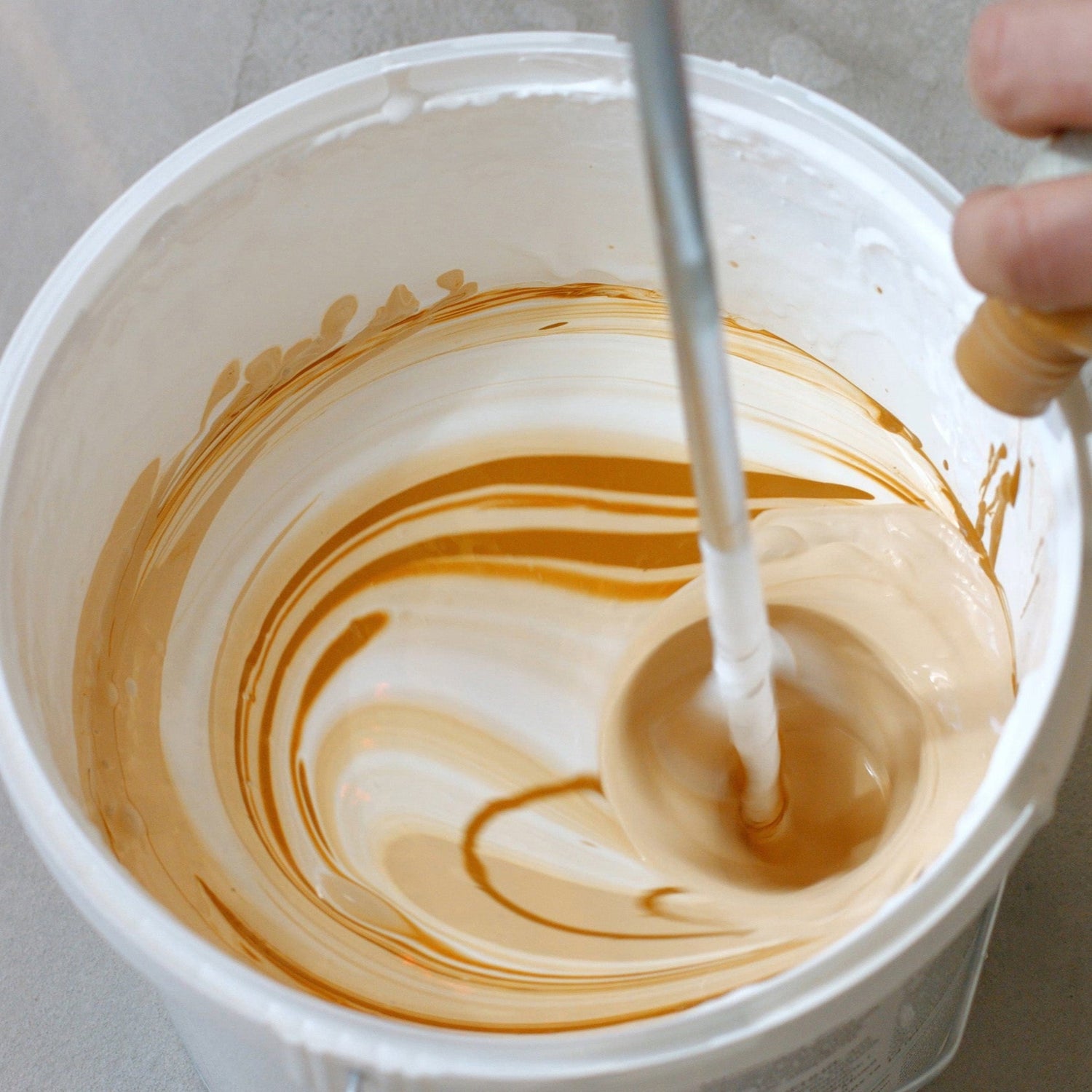 &lt;Hand of a manufacturing operator adding a brown liquid from a bottle to a white cream in a white bucket with an air propellor mixer causing a vortex and swirls of colour. Credit&gt; AdobeStock_269910716