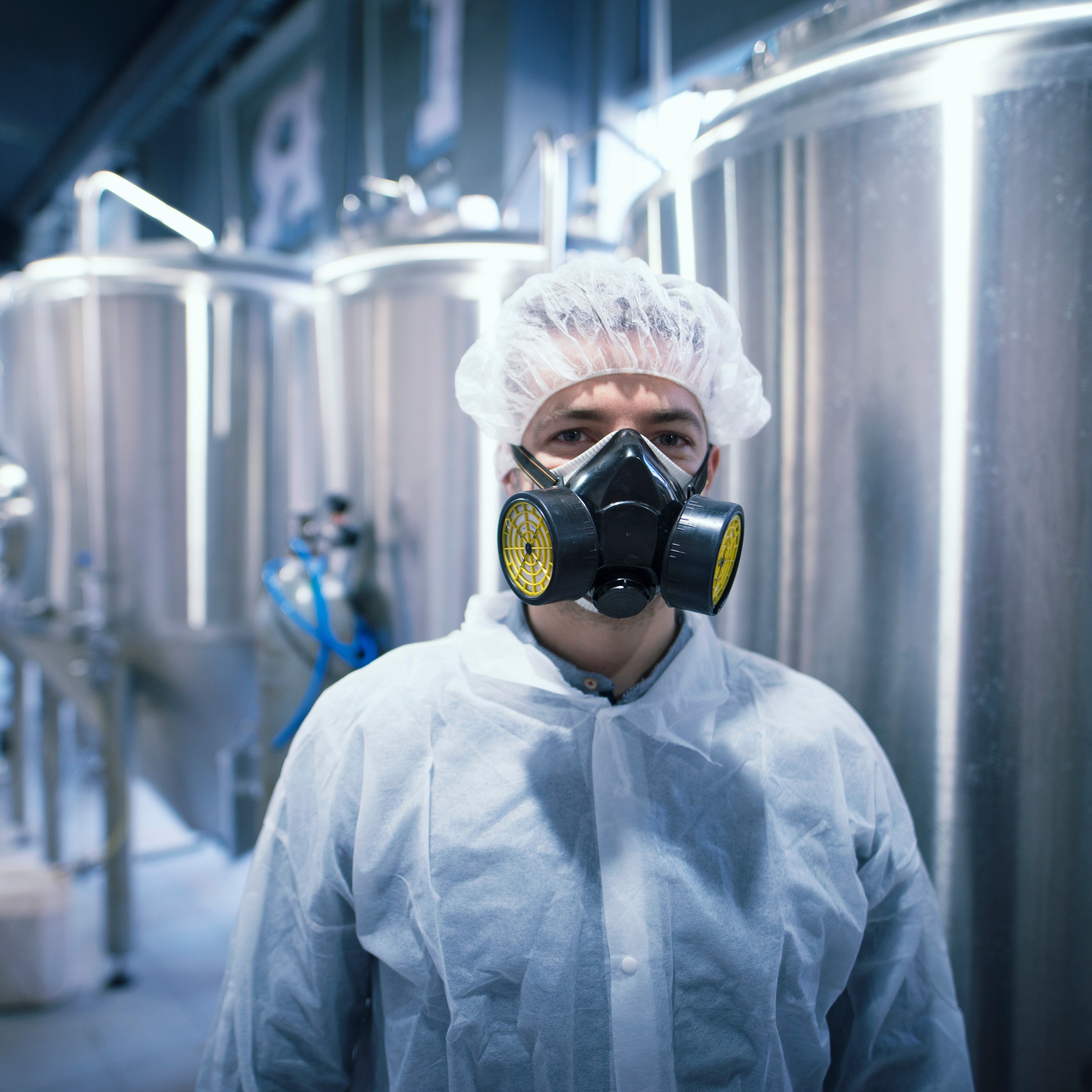 &lt;White male production operator stood in a manufacturing area of mixing tanks wearing a white coat and hairnet with a protective dust mask covering his nose and mouth. Credit&gt; AdobeStock_271852211