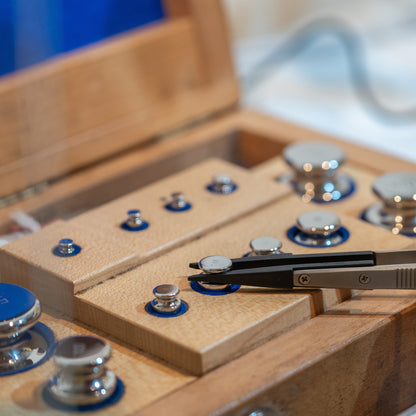 &lt;Tweezers picking up a chrome calibration weight for an analytical balance from a wooden box set of standard weights. Credit&gt; AdobeStock_274078427