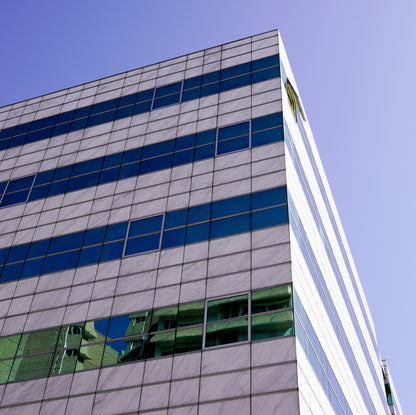 &lt;Looking up at the corner of a grey, blue, and glass striped company office building or laboratories with sunny blue sky. Credit&gt; AdobeStock_291035917