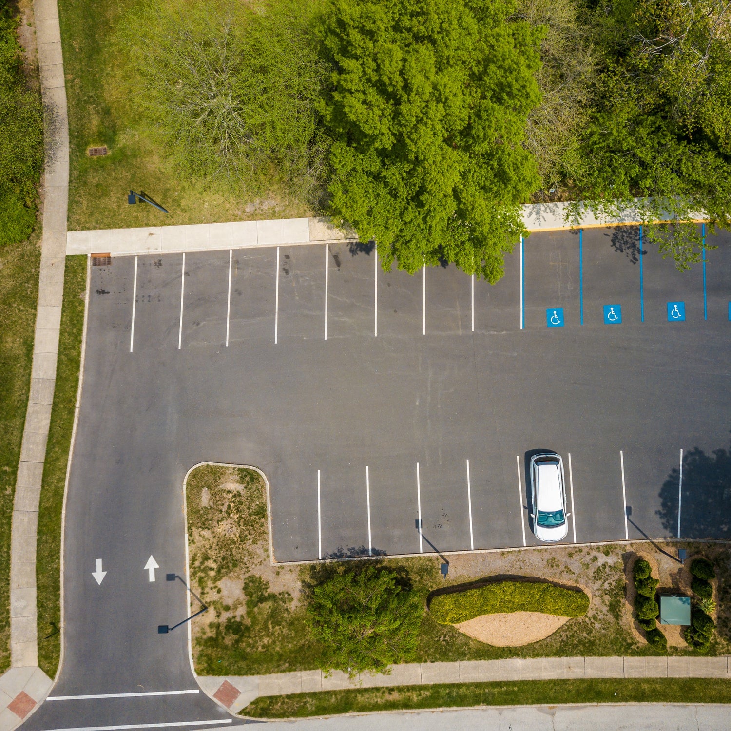 &lt;Employee tarmac car park or parking lot of 20 spaces and 4 disabled driver spaces with one white car surrounded by grass, trees and pathways. Credit&gt; AdobeStock_294267869