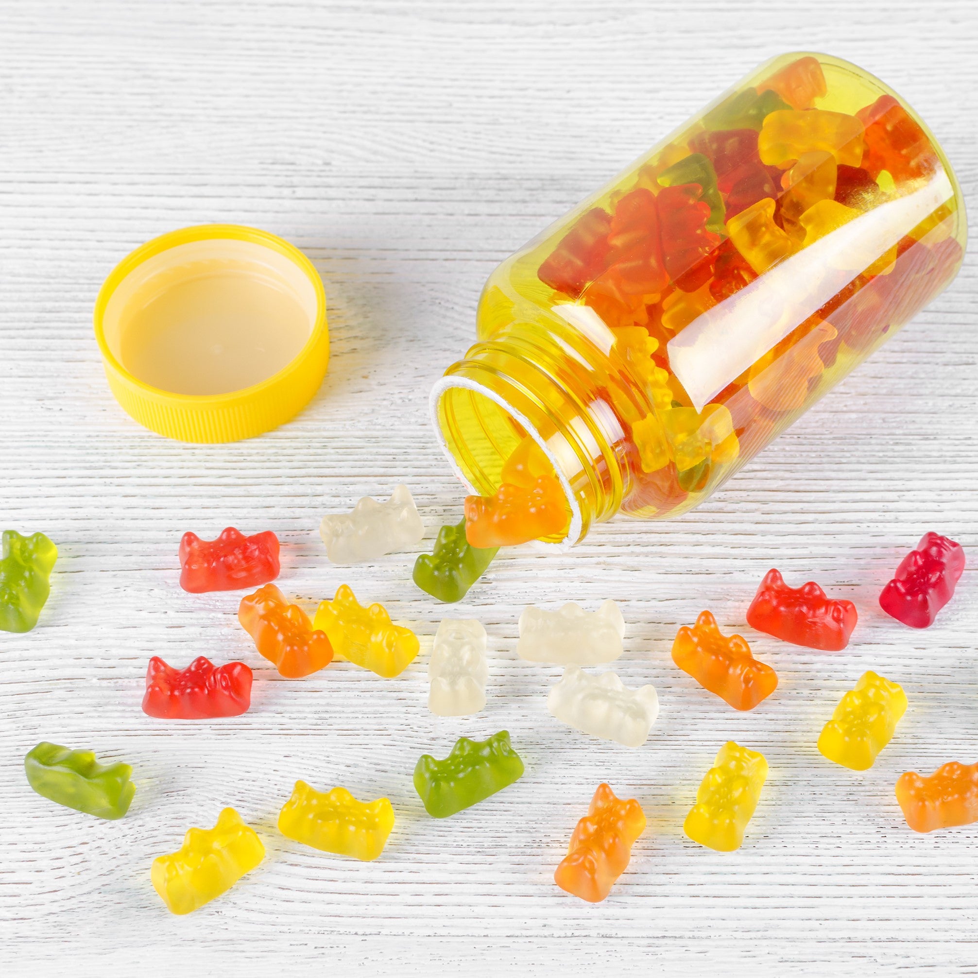 &lt;Clear, yellow plastic bottle, with opaque yellow lid, on its side with 15 red, orange, yellow, and green gummy bears tipped out on to a white woodgrain effect table. Credit&gt;  AdobeStock_301147051 