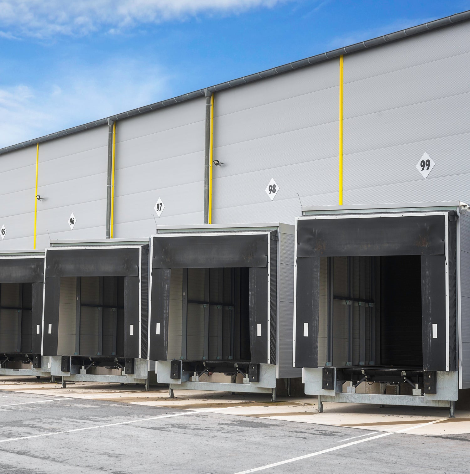 &lt;From the concrete yard for distribution, four loading bay doors in the side of a grey metal warehouse at lorry height and shape numbered 95 to 99. Credit&gt; AdobeStock_326508468