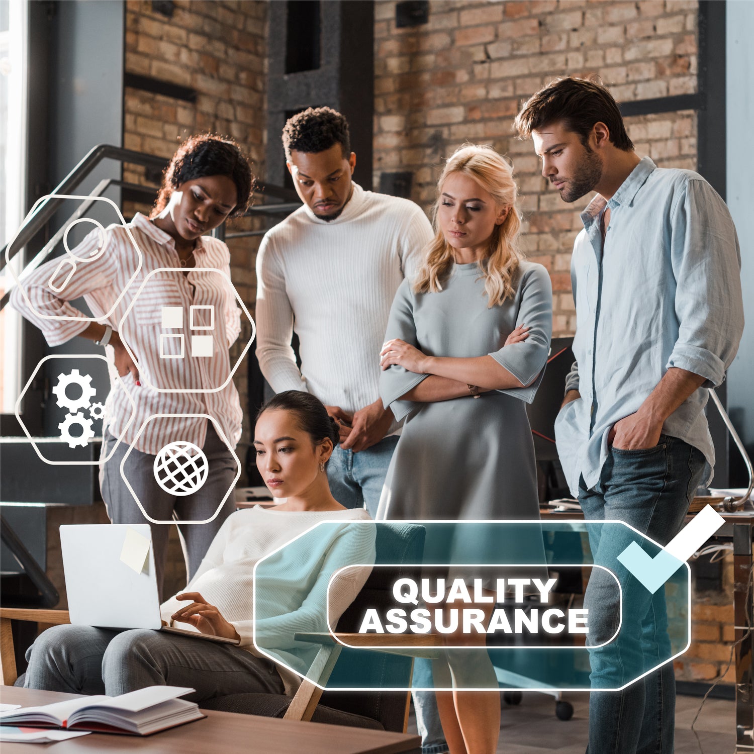 &lt;Four employees stood in an office with brick walls and grey metal window frames and stairs, reviewing something on the laptop of a fifth employee sitting down typing with Quality Assurance on her screen. Credit&gt; AdobeStock_334496432