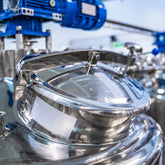 <Close up of the lid of a polished mirror finish stainless steel mixing tank with overhead blue motor driving the stirrer. Credit> AdobeStock_336493389