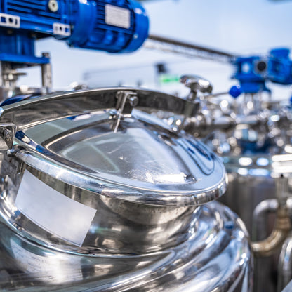 &lt;Entry port or lid of a polished, mirror finish, stainless steel mixing vessel or tank, with an overhead blue mixer or homogenizer with another in the background. Credit&gt; AdobeStock_336493389