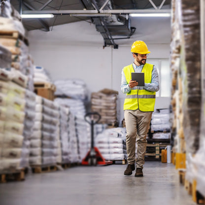 &lt;Warehouse supervisor, wearing fluorescent yellow jacket and hard hat, walking along an aisle checking pallets of deliveries of materials in sacks with an ipad. Credit&gt; AdobeStock_349770975