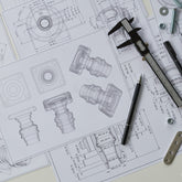 <Technical 3D drawings of equipment parts with measuring calipers, pens and nuts and bolts sitting on top. Credit> AdobeStock_354937079