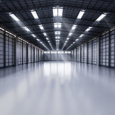 <Completely empty warehouse building with perfect grey non-slip floor, grey walls with black square frames, and black metal roof with 5 rows of skylights. Credit> AdobeStock_360611578