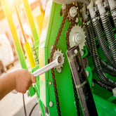 <Arm of a Maintenance Engineer tightening the chain on the gears of a  green coloured filling machine with a socket spanner. Credit> AdobeStock_362397816