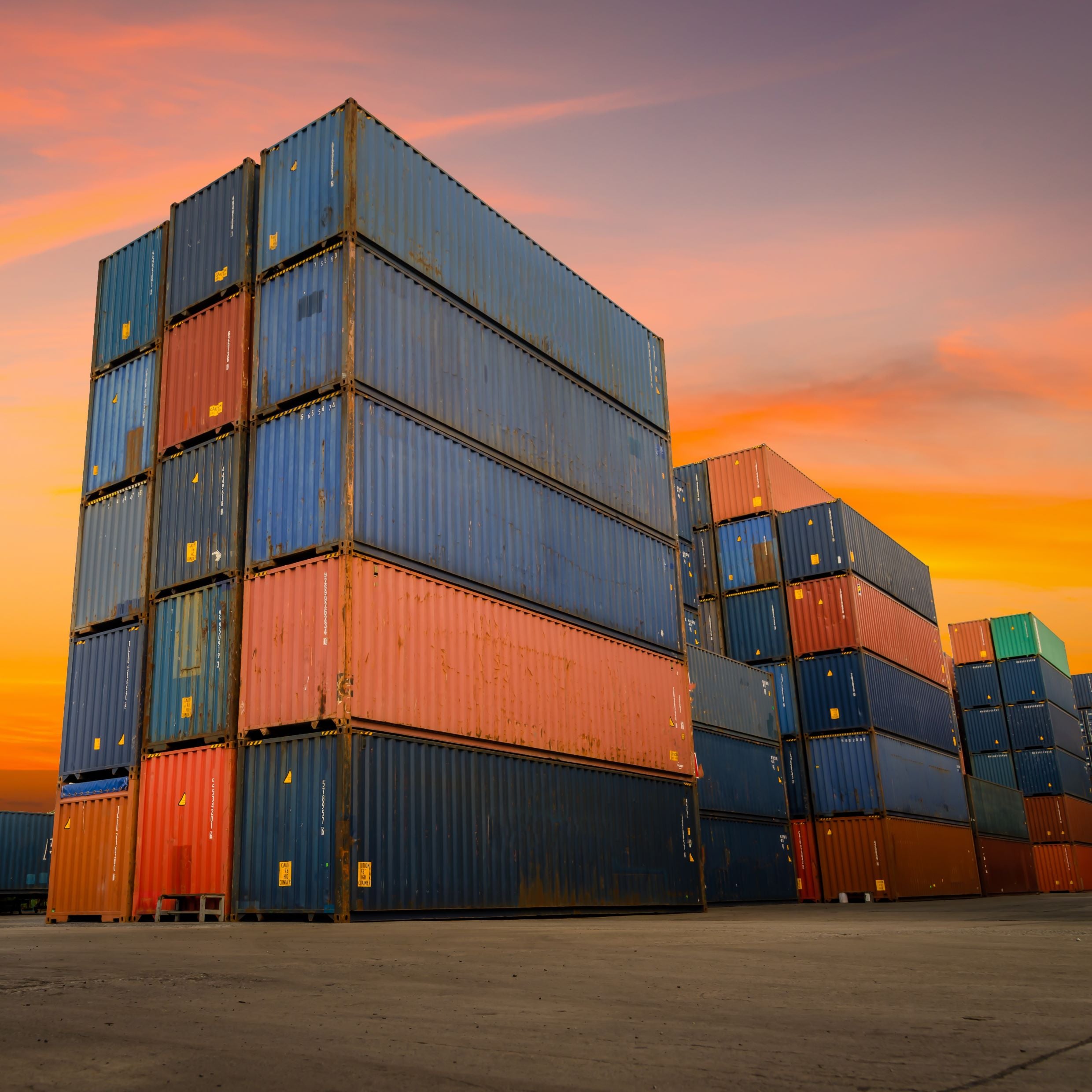 &lt;Stack of blue and orange shipping containers five high at a concrete port in winter sunset ready to be distributed by sea. Credit&gt; AdobeStock_377498722