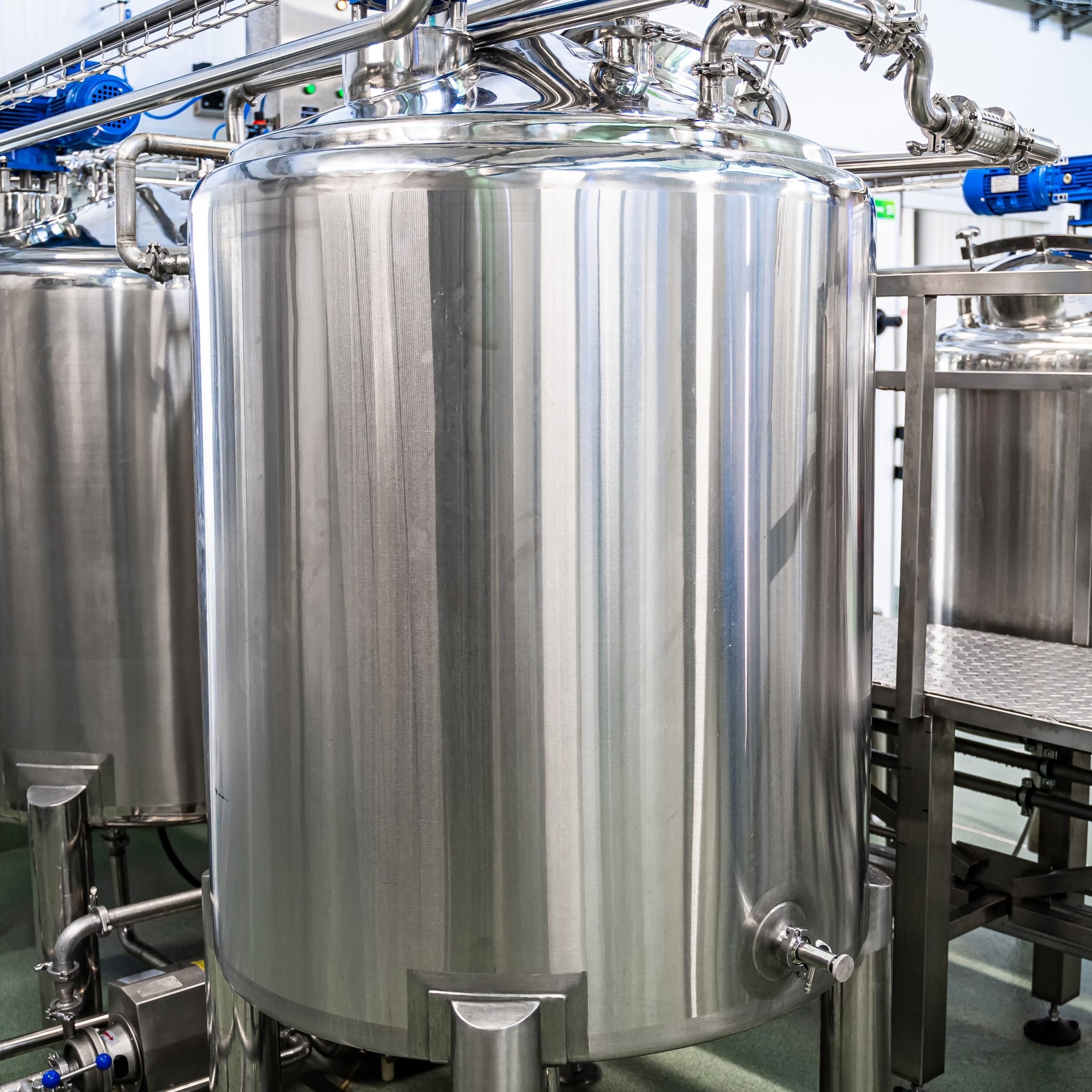 &lt;Several large, cylindrical, shiny stainless steel  mixing tanks and pipework in a dietary supplement manufacturing unit with gantry, grey non slip floor and white ceiling. Credit&gt; AdobeStock_383238064