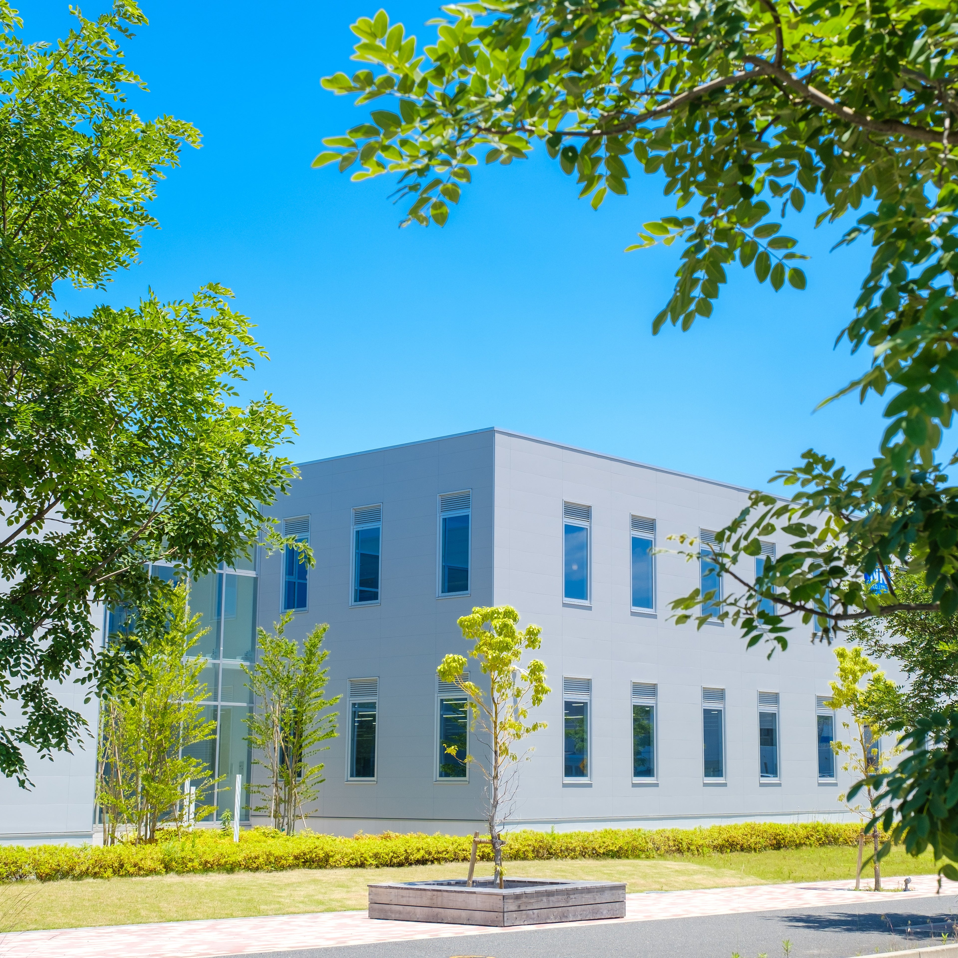 &lt;Outside of a grey metal and glass drug facility on a bright sunny day with well kept green spaces, pathways and trees. Credit&gt; AdobeStock_437323910