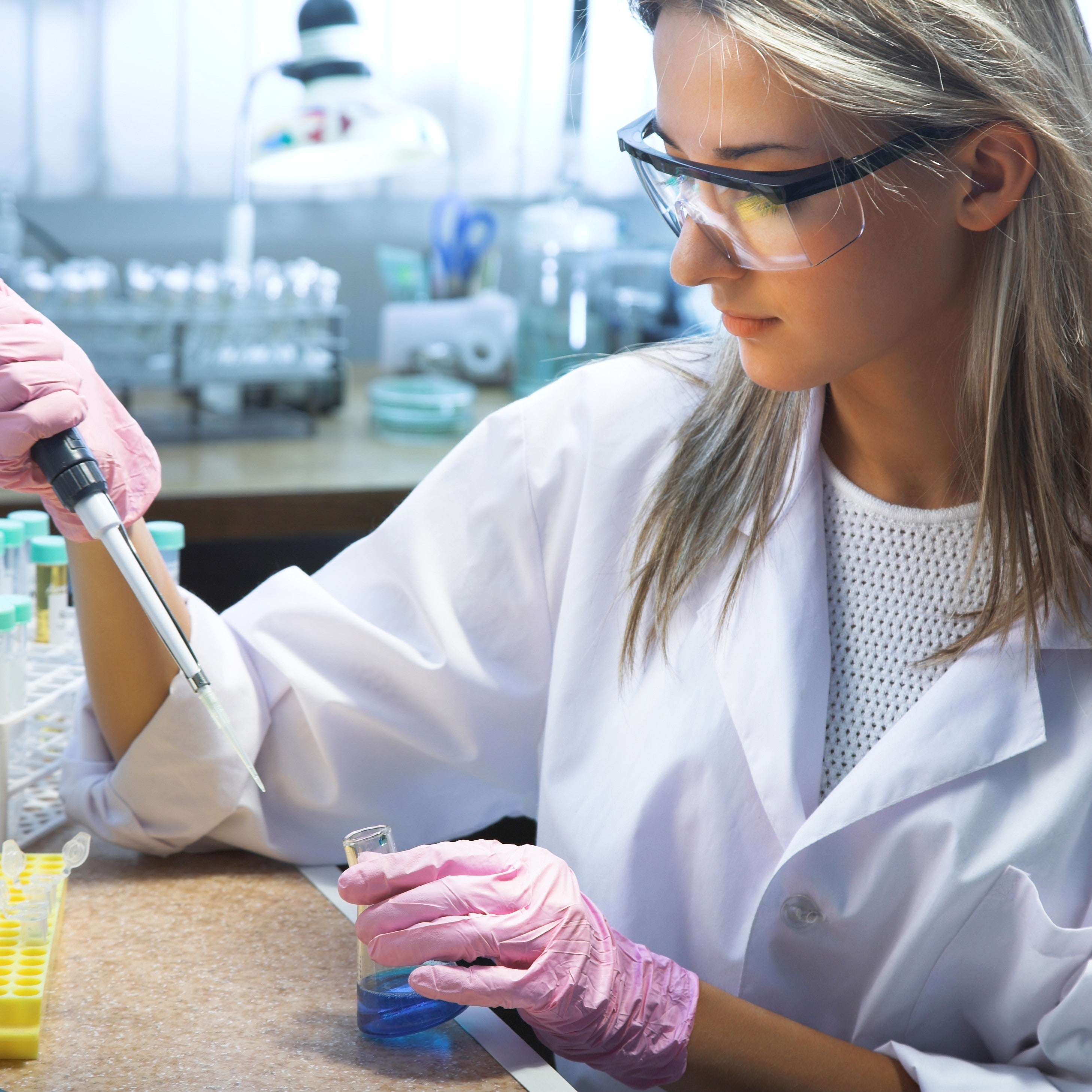 &lt;Female laboratory analyst wearing pink gloves pipetting into a conical flask of clear blue liquid. Credit&gt; AdobeStock_44142293