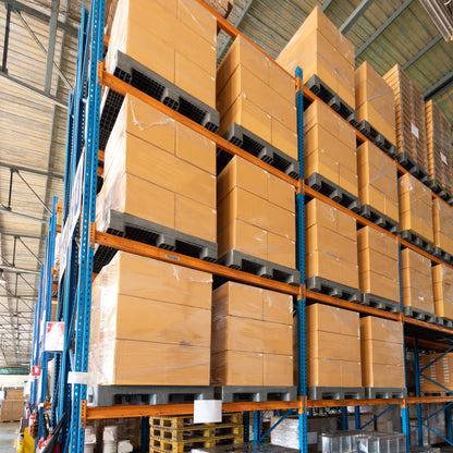 &lt;Rows of cardboard boxes of packaging materials on wooden pallets on orange and blue warehouse racking. Credit&gt; AdobeStock_477083814