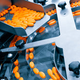 <Orange oval tablets passing down a stainless steel chute onto a rotary filling machine which is collating the tablets in larger circles into one aligned row. Credit> AdobeStock_477674087