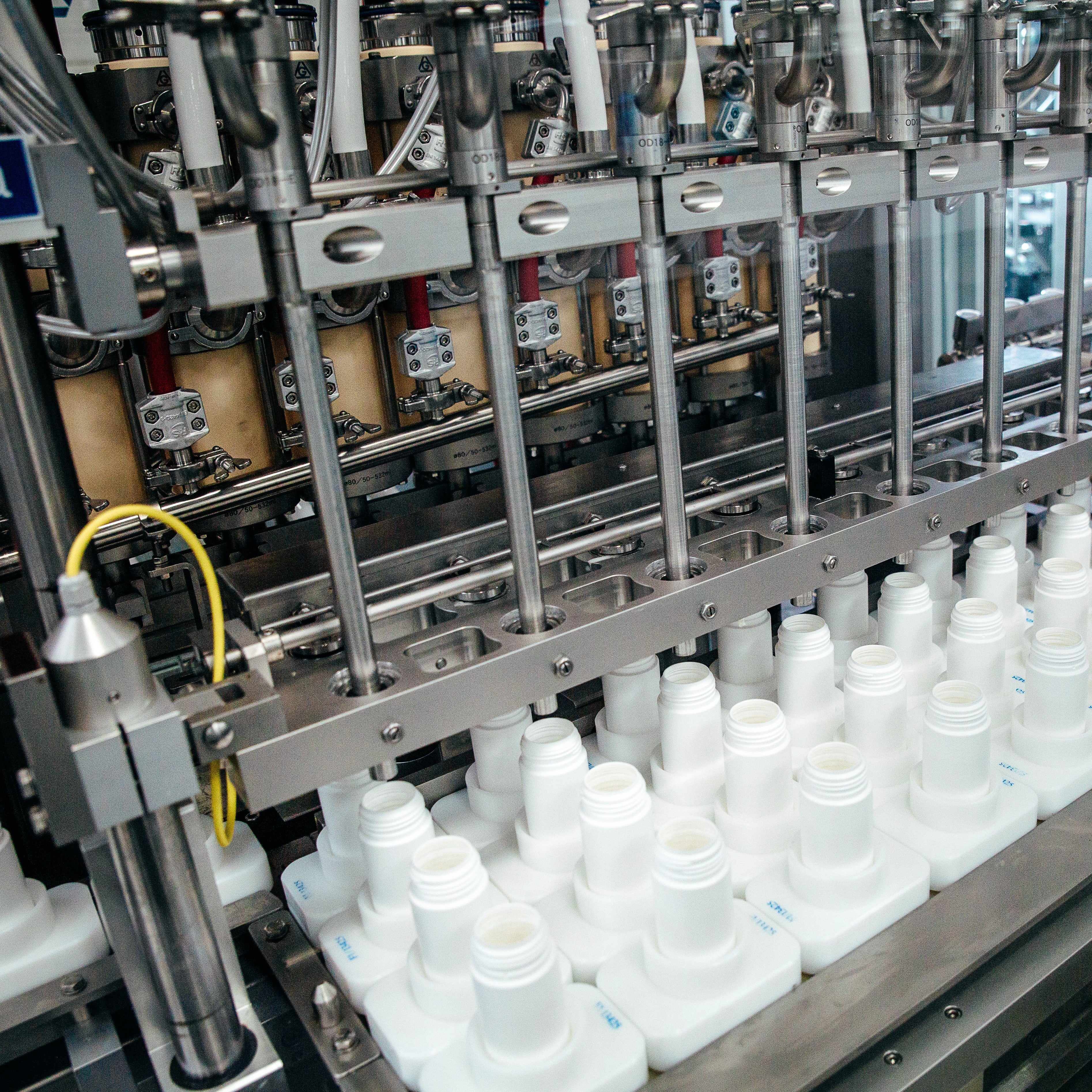 &lt;Four rows of white bottles on a conveyor belt being filled by a series of nozzles under GMP conditions on a production line. Credit&gt; AdobeStock_478344828