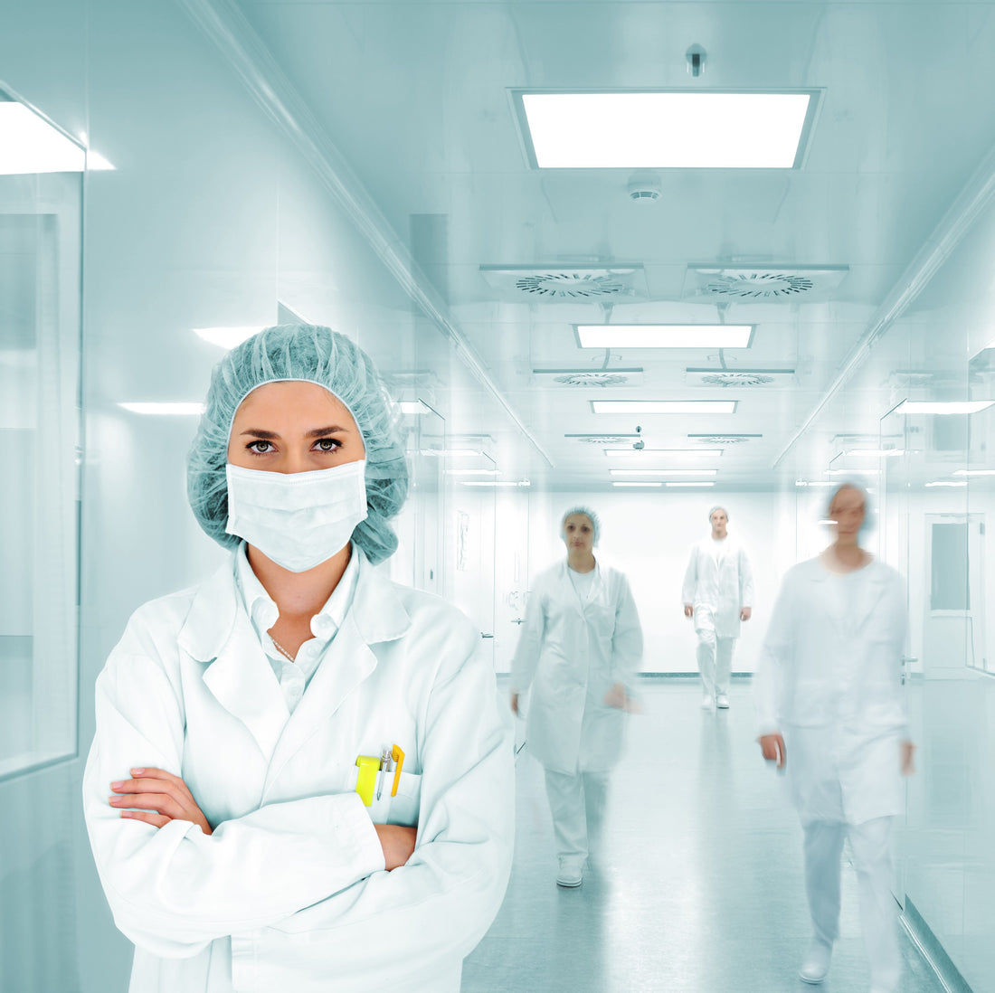 &lt;Four female employees at various distances away walking down a white corridor in production with a series of square ceiling LED lights, windows, and non slip floor, wearing white overalls and blue hairnets. Credit&gt; AdobeStock_49725046