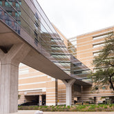 <Concrete and glass bridge walkway between two buildings in a drug facility above a road and garden space. Credit> AdobeStock_523238820