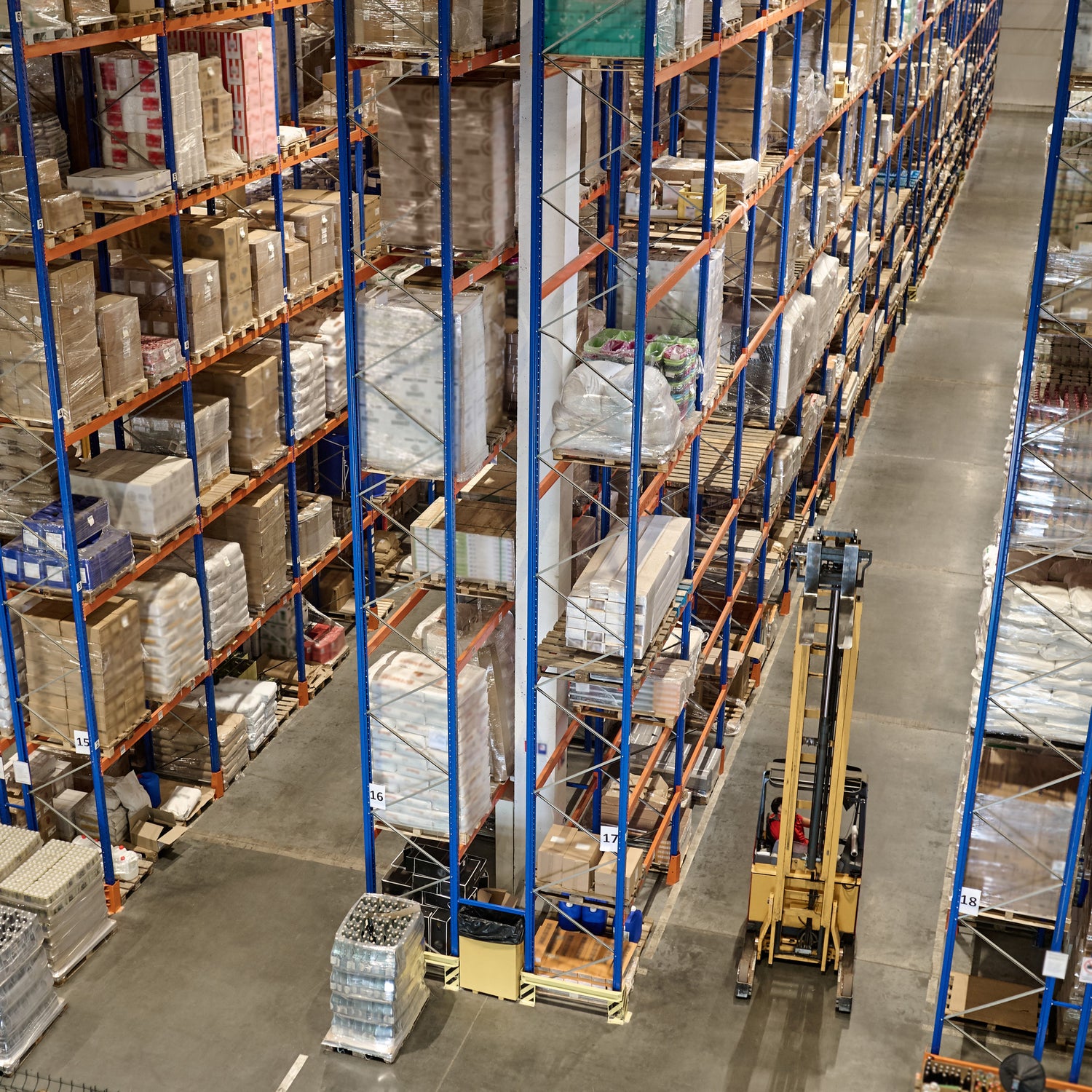 &lt;View from the ceiling looking down into clean, tidy warehouse to see a yellow forklift truck on concrete floor operating between rows of racking containing boxes and sacks of materials. Credit&gt; AdobeStock_544570194