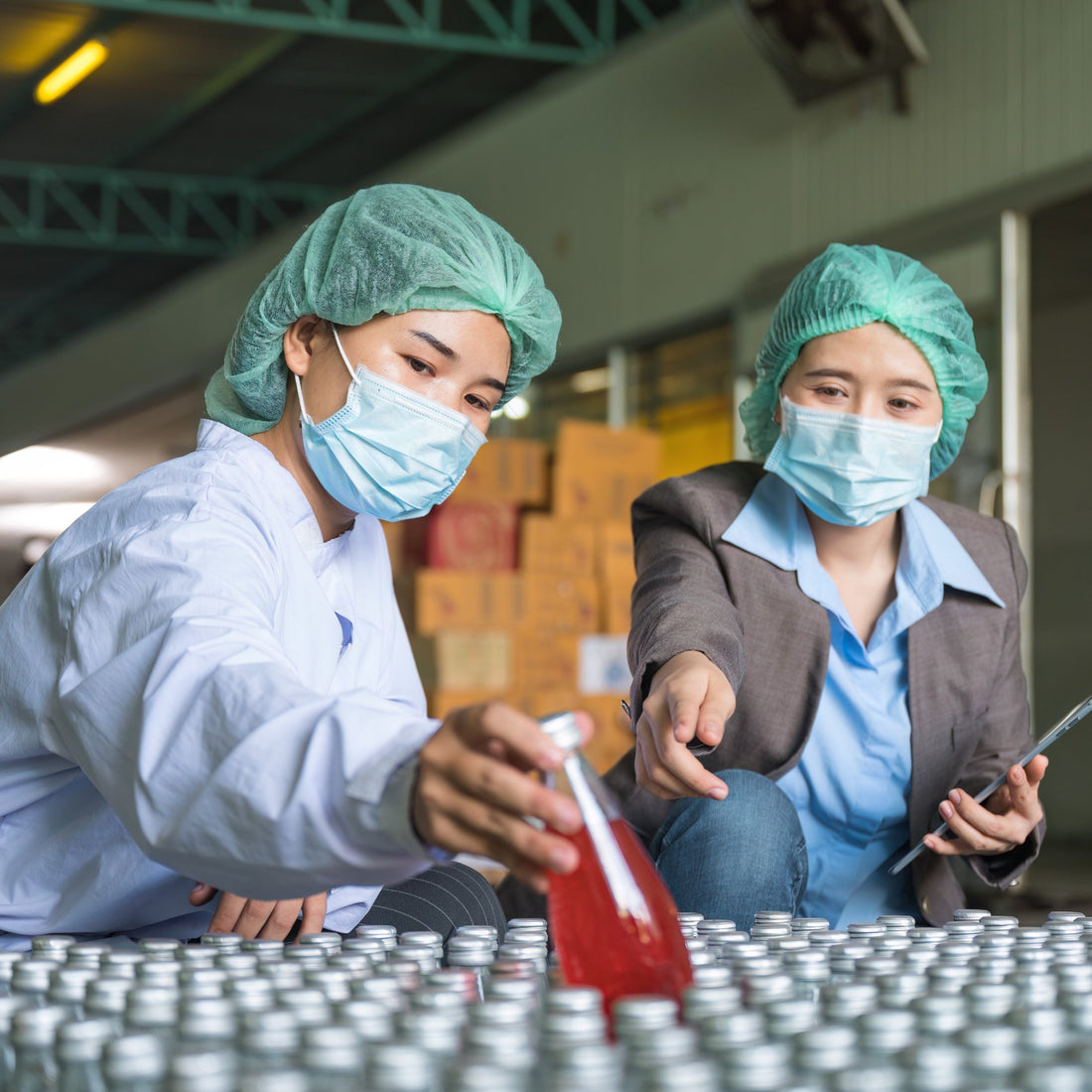 &lt;A female Quality Assurance Officer reviewing dietary supplement bottles filled with red liquid with a female Production Team Leader, both wearing blue hairnets and face masks. Credit&gt; AdobeStock_551742643