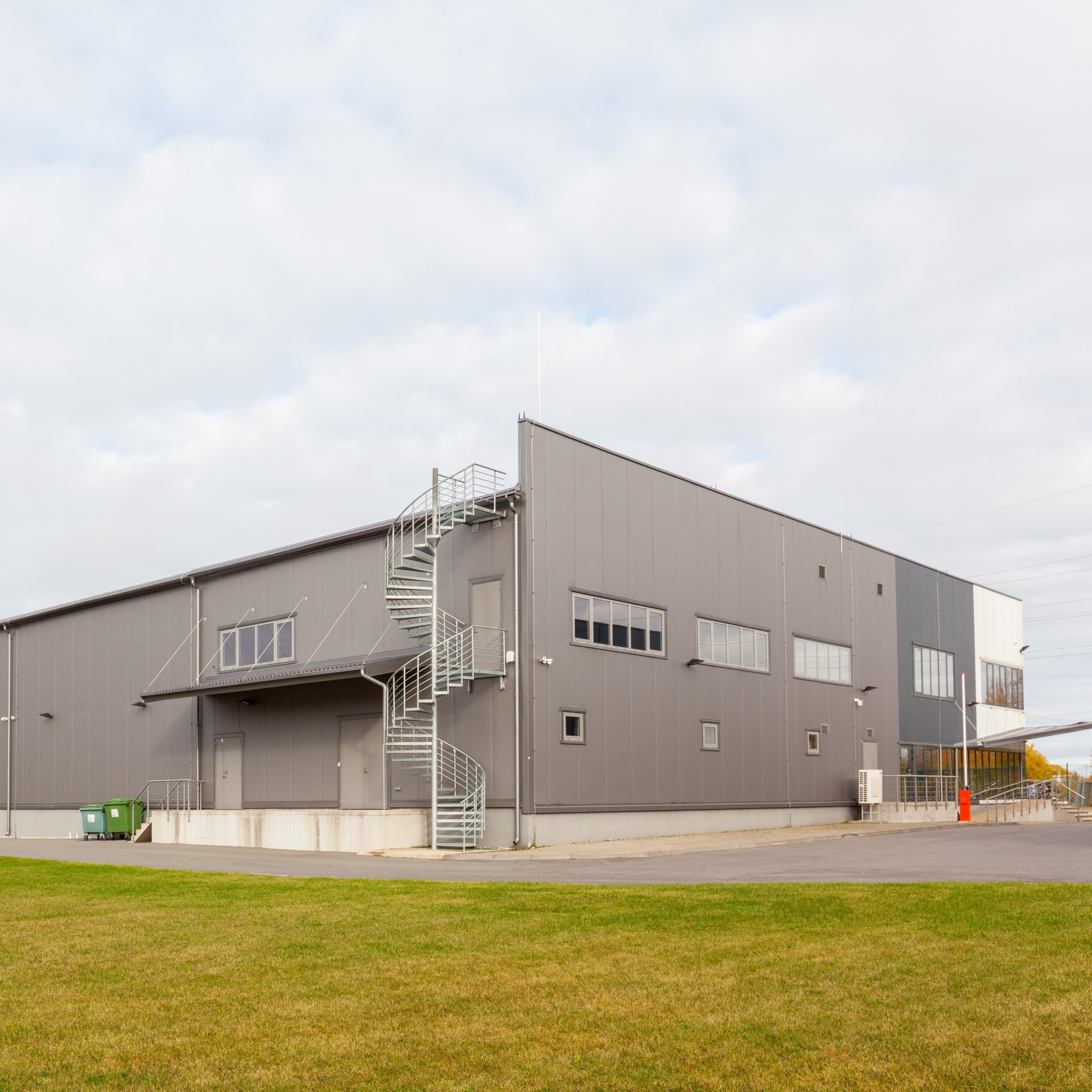 &lt;Looking across a well kept grass area and tarmac yard to a grey metal drug facility with a row of first floor windows and a spiral fire escape from the roof. Credit&gt; AdobeStock_564629963