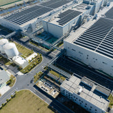 <Overhead photograph of a dietary supplement facility with three large buildings with solar panels, two large cylindrical storage tanks, roads and green spaces. Credit> AdobeStock_569070113