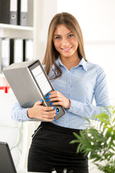 <Female employee next to a laptop, wearing blue shirt and black skirt, holding a box folder of dietary supplement records taken from a shelf behind her. Credit> AdobeStock_73250678