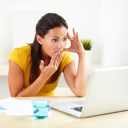 &lt;Woman wearing yellow top sitting at a table, with white background, looking shocked holding her hand to her mouth at an e-mail response to a complaint on a white laptop. Credit&gt; AdobeStock_78493419