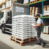 <Male warehouse operator receiving a delivery note and wooden pallet loaded with 20 Kg white sacks of powdered materials next to some racking with cardboard boxes. Credit> Freepik