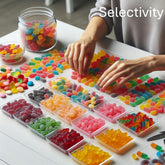 <Representing Selectivity, female hands, wearing grey jumper, sorting hundreds of multi coloured pillow shaped gummies,  arranged in small clear plastic trays five by five, on a white table, by colour and design. Credit> Freepik