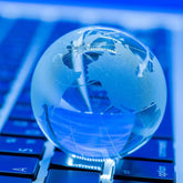 <Clear and etched glass globe of the world sat on a blue computer keyboard representing world trade. Credit> Freepik