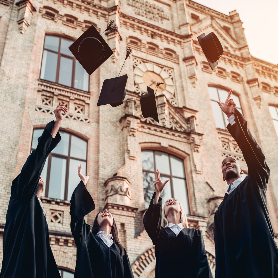 &lt;Four university college graduates, two male and two female, stood outside the university wearing graduation gowns throwing their mortarboard hats in the air in celebration of qualifying. Credit&gt; 98006981 © Vasyl Dolmatov | Dreamstime.com