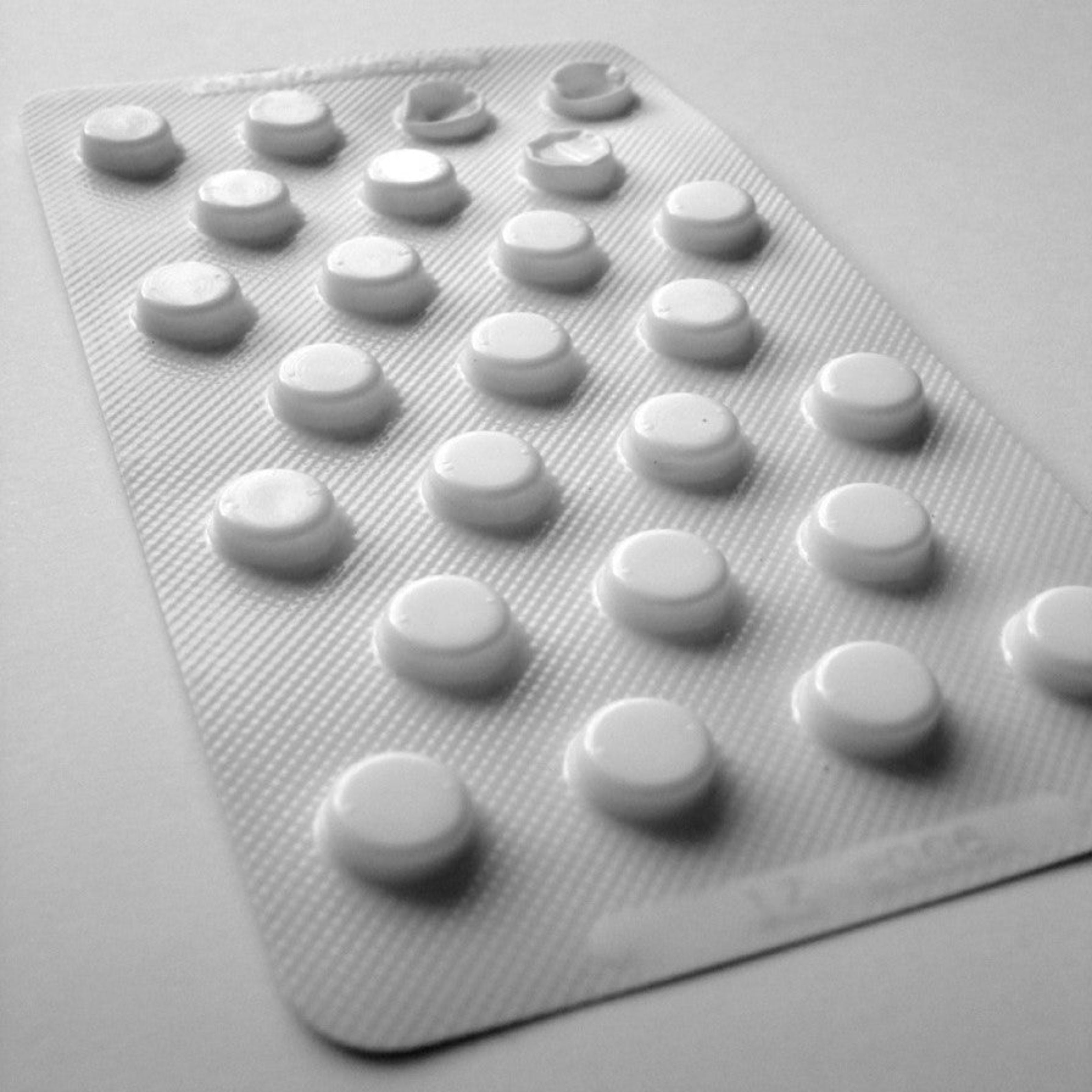 &lt;Close up of a white plastic foil blister sheet containing 25 tablets where 3 from the top right hand corner have been pressed out and used, sitting on a white surface. Credit&gt; 1328288 by secureroot @ freeimages