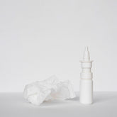 <White plastic nasal spray bottle on a white surface next to a crumpled used white tissue. Credit> Freepik