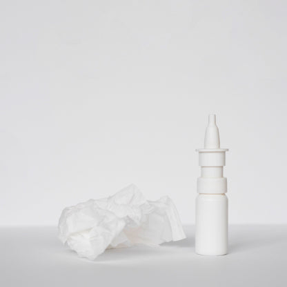 &lt;White plastic nasal spray bottle on a white surface next to a crumpled used white tissue. Credit&gt; Freepik